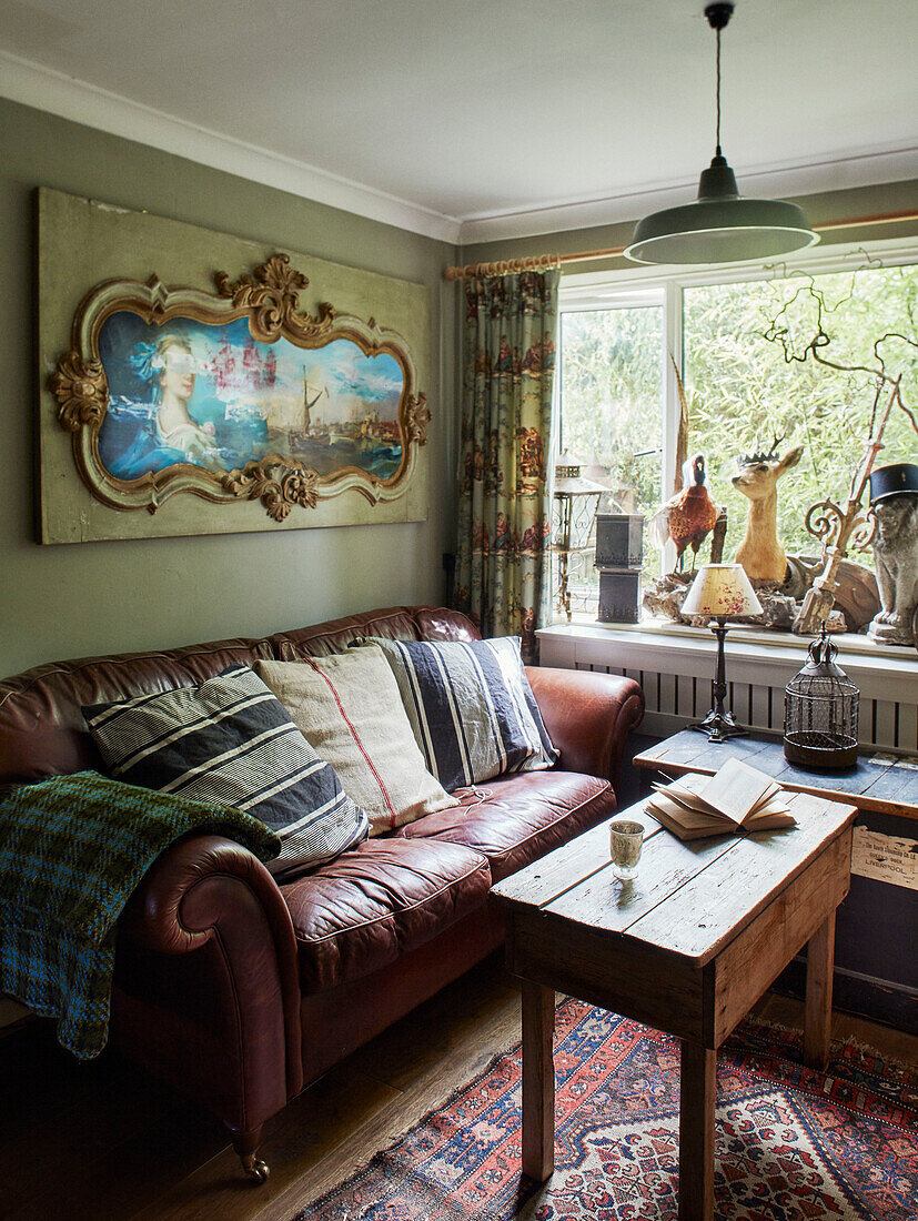 Ornaments on windowsill with brown leather sofa and wooden table in Somerset home, UK