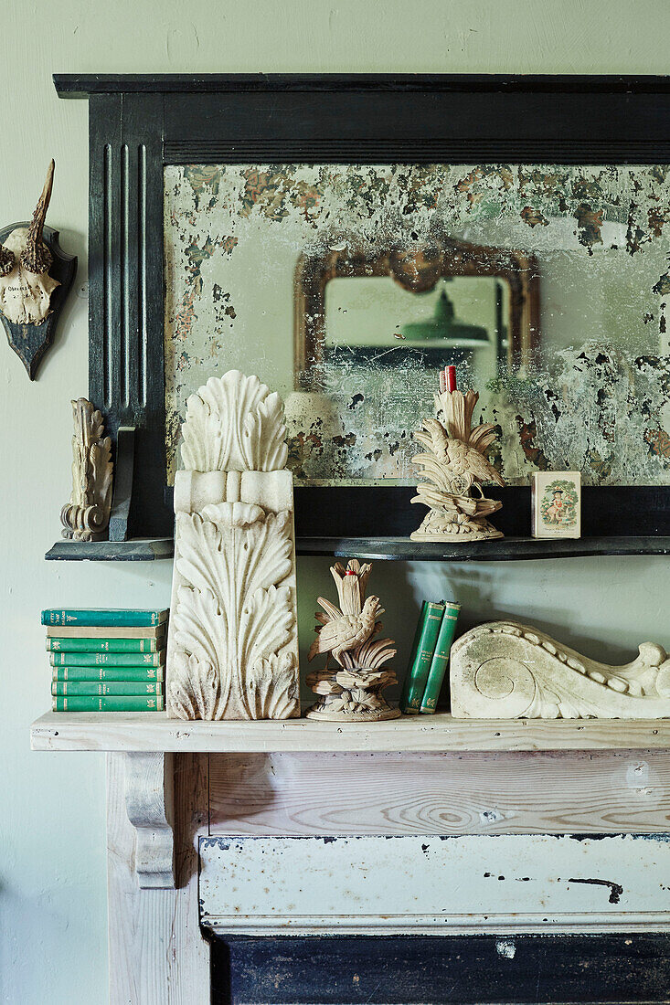 Green books and ornaments with antique mirror on Somerset mantlepiece, UK