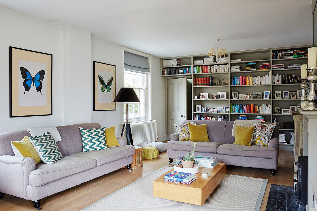 Butterfly prints and sofas with bookcase in Oxfordshire living room, UK