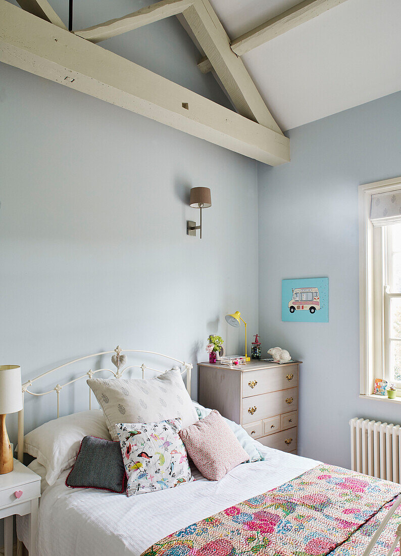 Cushions and covers on bed in light blue girl's room with beamed ceiling Oxfordshire, UK