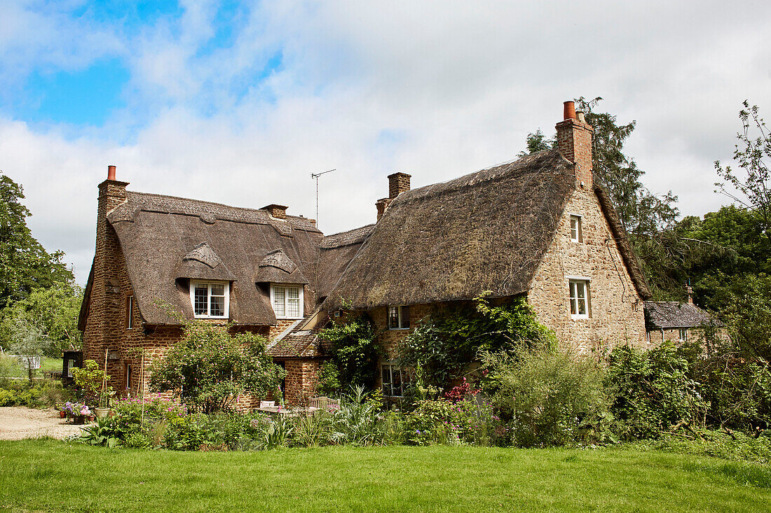 Begrünter Garten vor einem reetgedeckten Bauernhaus in Oxfordshire, UK
