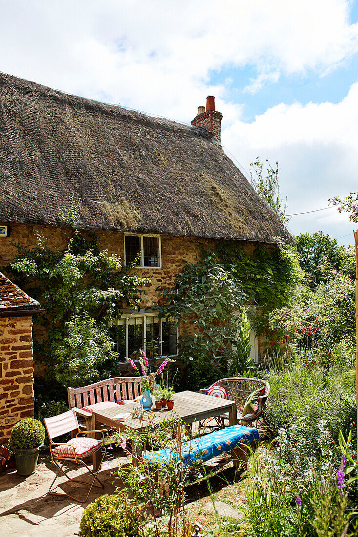 Terrassenmöbel vor einem traditionellen reetgedeckten Cottage in Oxfordshire, UK