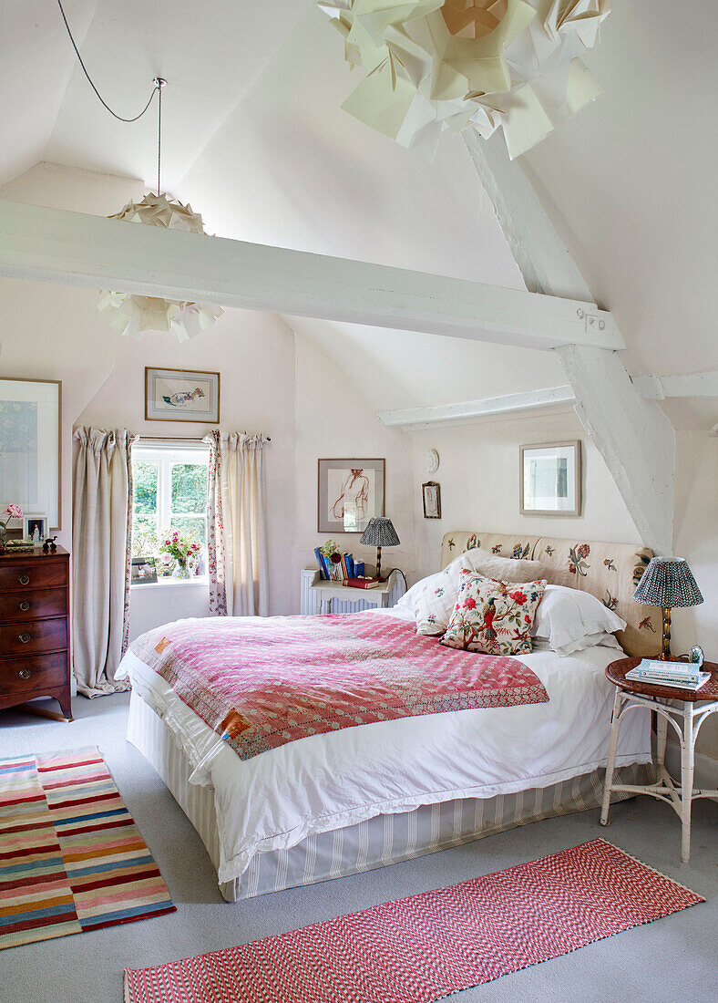 Doppelbett mit gemusterten Teppichen und hoher Decke in einem Bauernhaus in Oxfordshire, UK