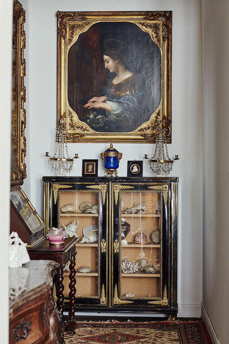 Gilt framed artwork above display cabinet with shells in Foix townhouse Ariege, France