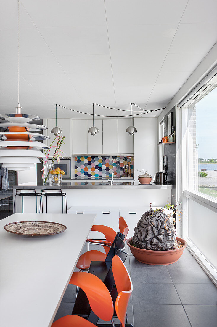 Dining table and orange chairs in front of modern, open-plan kitchen