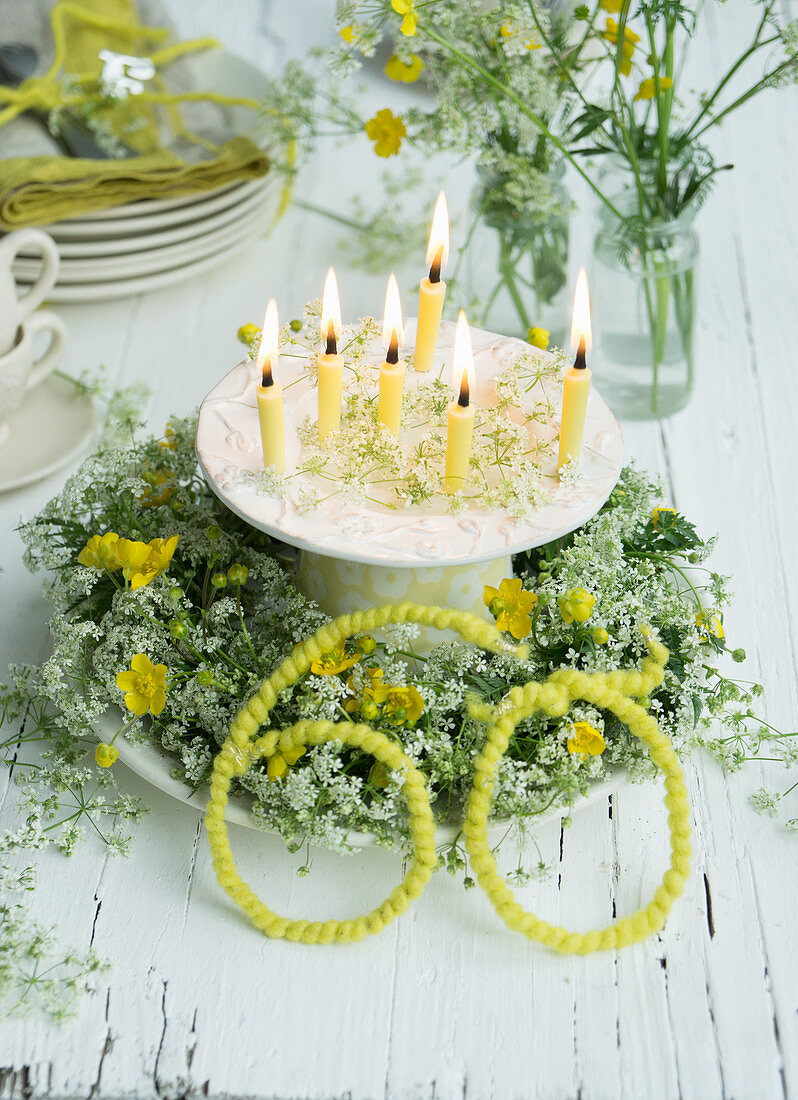Wreath of cow parsley and buttercups on plate around candles on cake stand for 60th birthday
