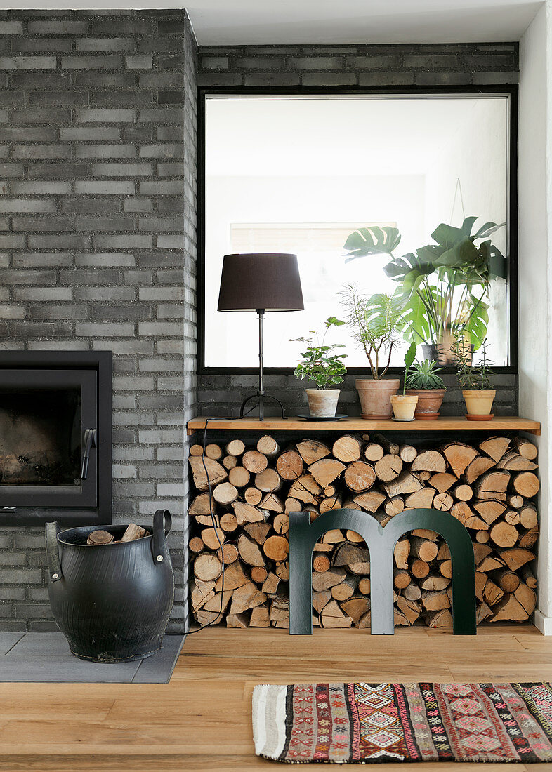 Buchstabe M vorm Brennholzstapel unterm Fenster mit Pflanzen