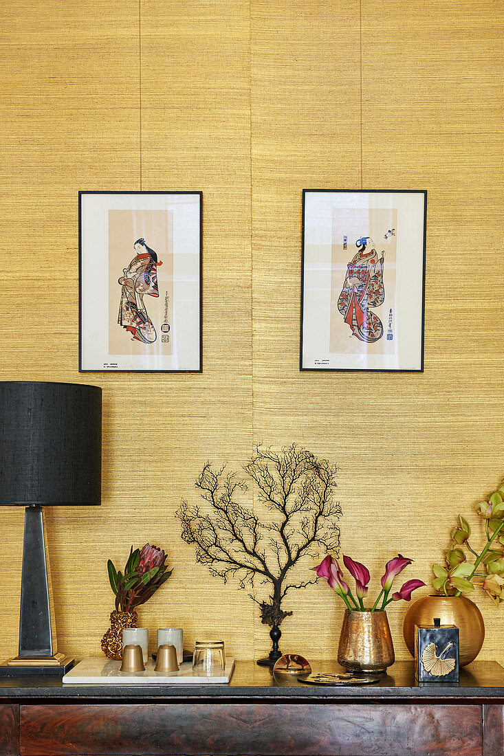 Japanese prints above golden ornaments and corals against grasscloth wallpaper