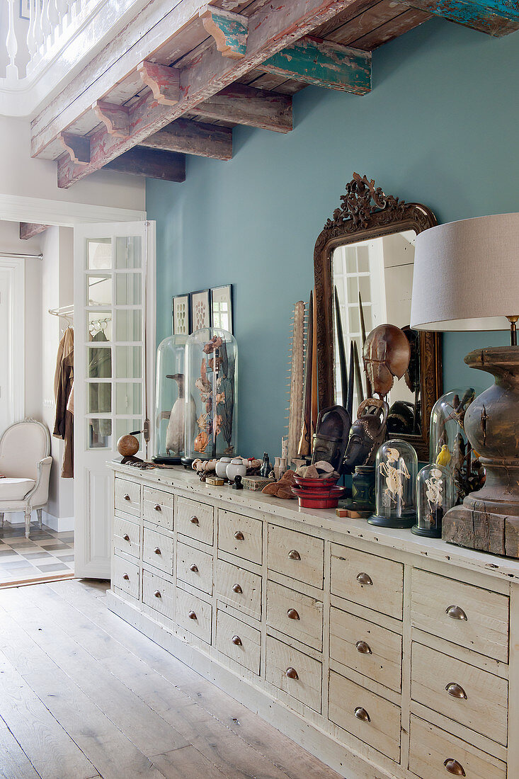 Collection of curiosities on sideboard with drawers against blue wall