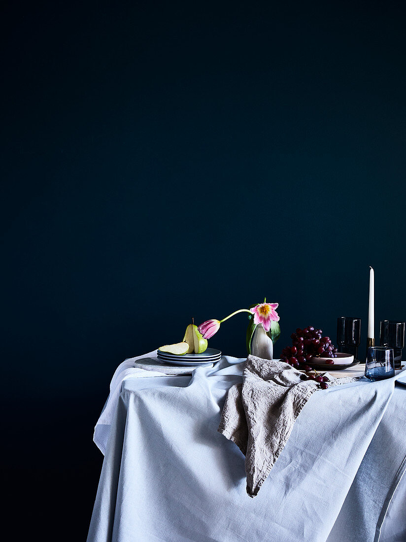 Esstisch mit heller Tischdecke, Birne, Blume und Weintrauben
