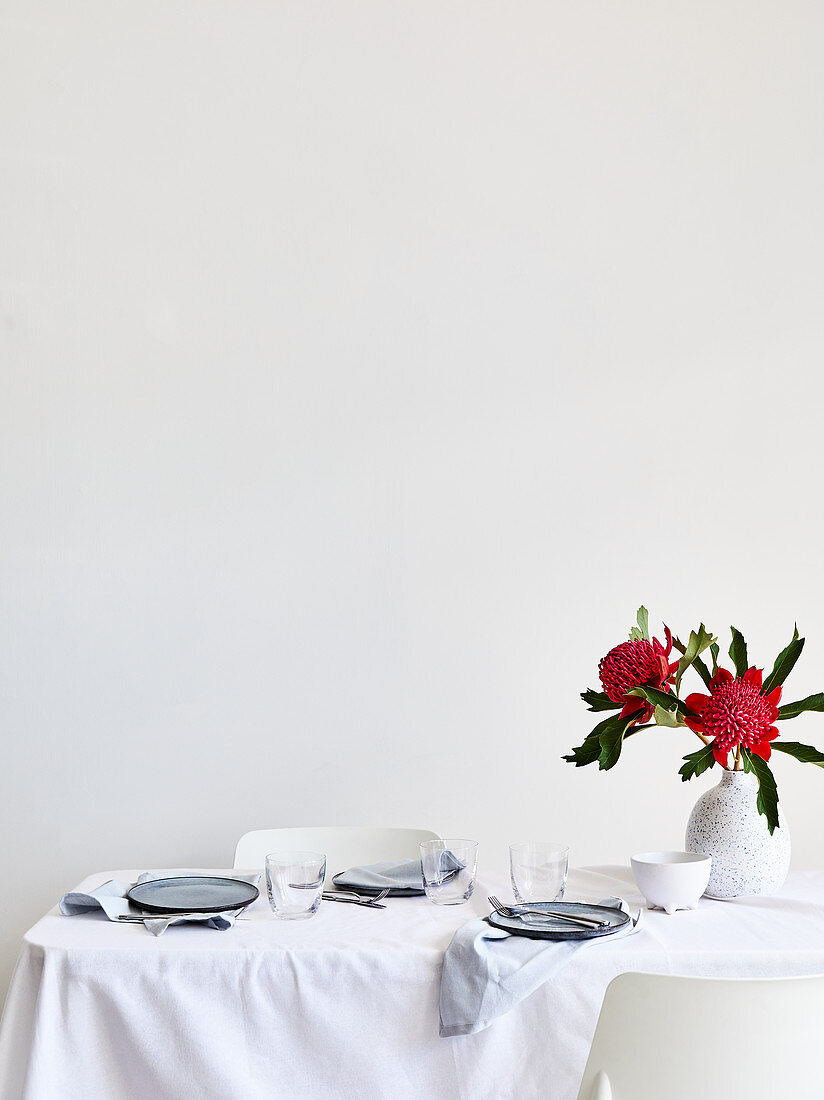 Gedeckter Tisch mit weißer Tischdecke und roten Blumen