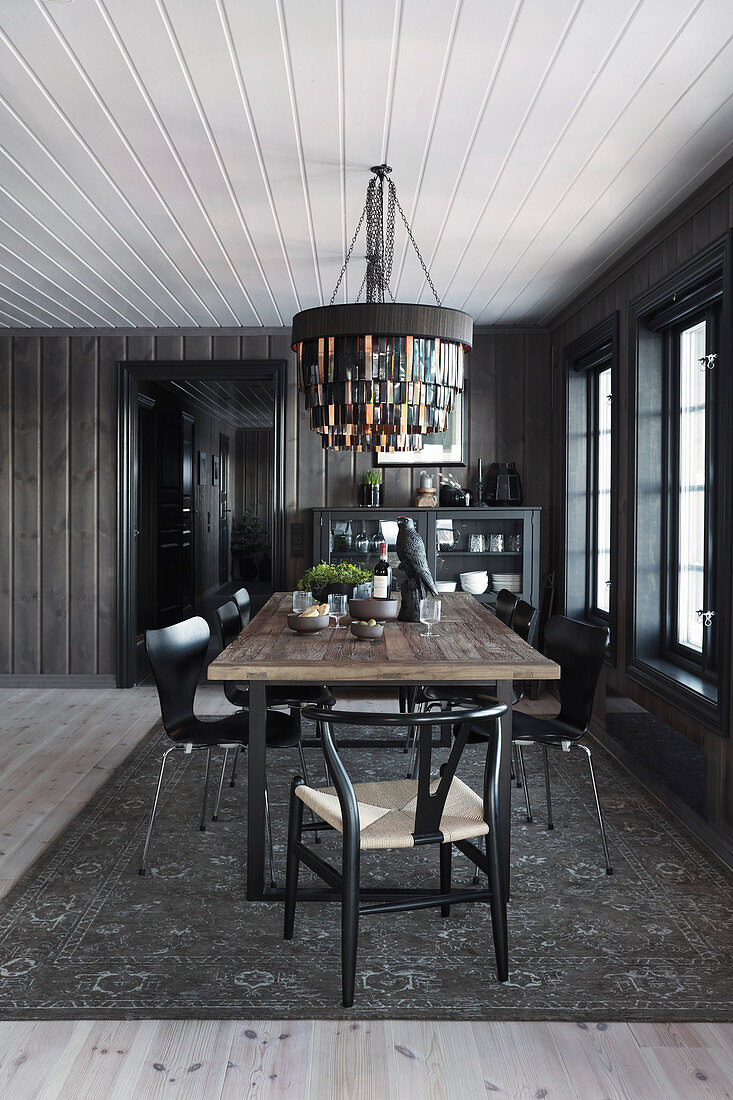 Designer chairs around dining table in wooden house decorated in black and grey