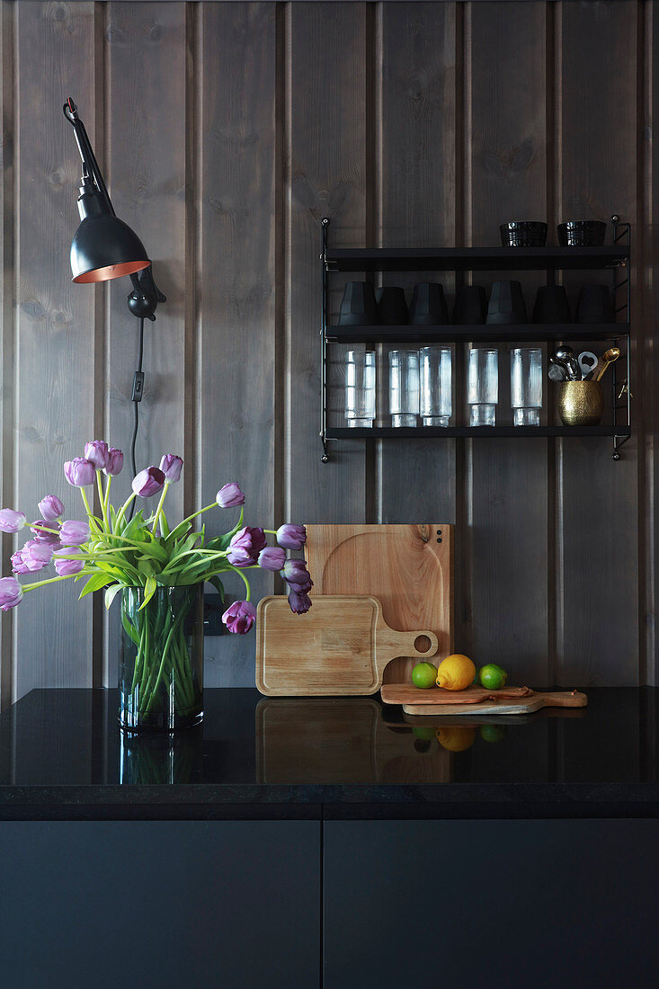 Vase of tulips on black kitchen counter against wood-clad walls
