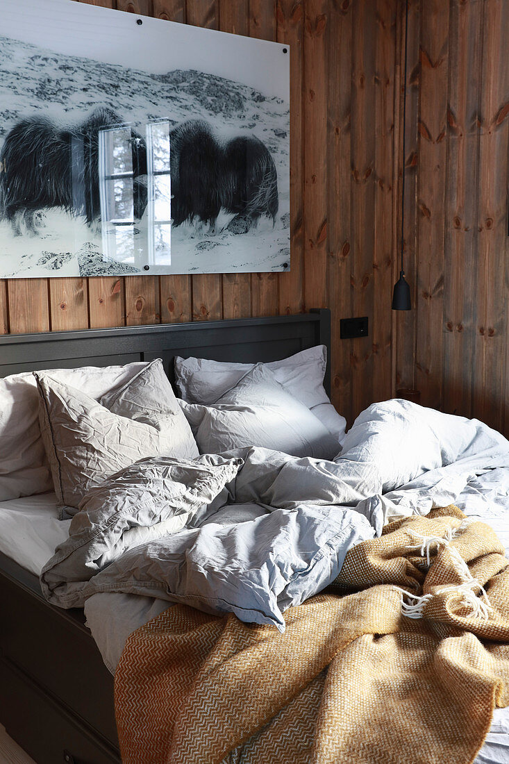 Zerwühltes Bett im gemütlichen Schlafzimmer mit Wandverkleidung