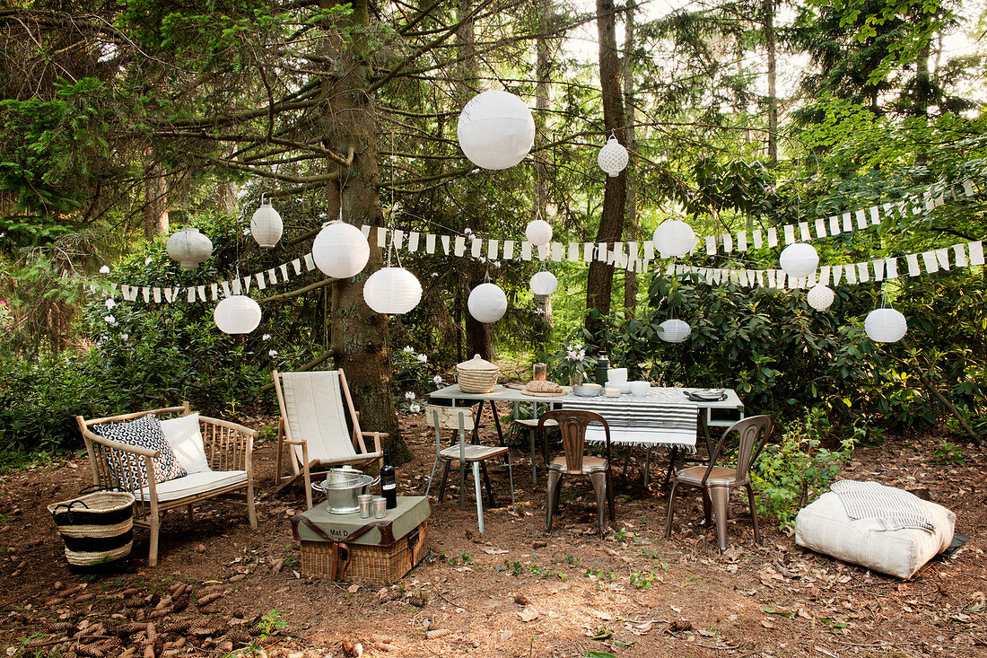 Tisch mit Stühlen, verschiedene Sitzmöglichkeiten und Partydekoration auf Waldlichtung