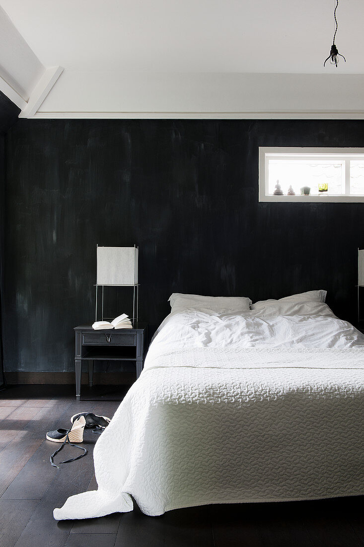 Doppelbett mit weißer Bettwäsche vor schwarzer Wand