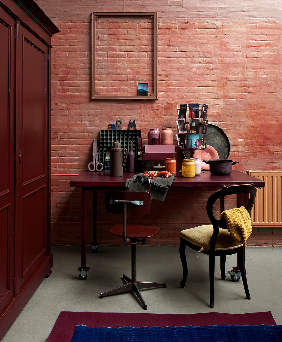 Schreibtisch mit Stühlen vor rotbrauner Ziegelwand, daneben Holzschrank
