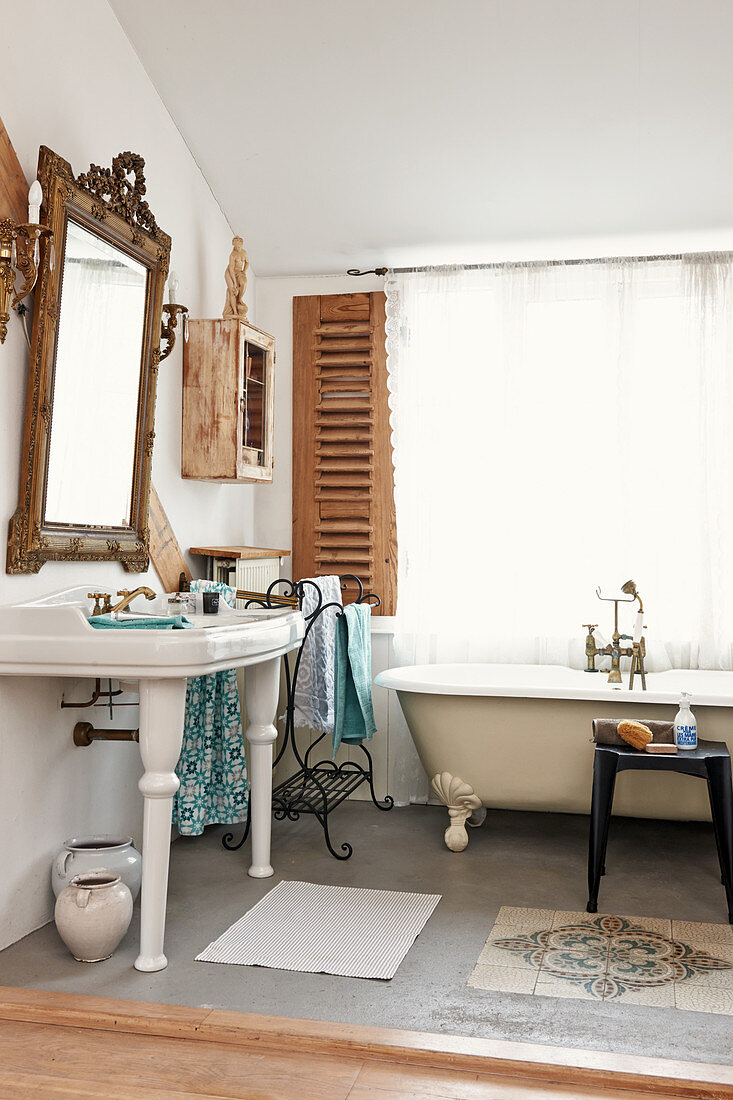 Vintage Standwaschbecken unter gerahmtem Spiegel und Badewanne vor Fenster
