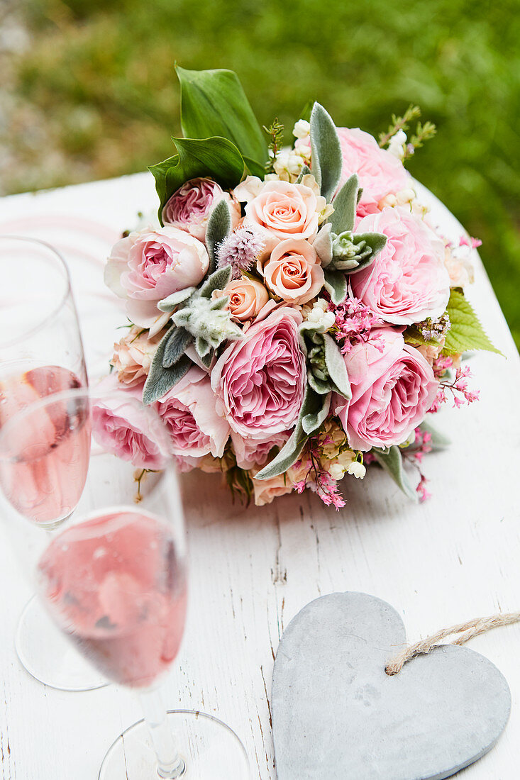 Lavish bouquet of roses, lily-of-the-valley and lamb's ear, glasses of pink Champagne and heart pendant