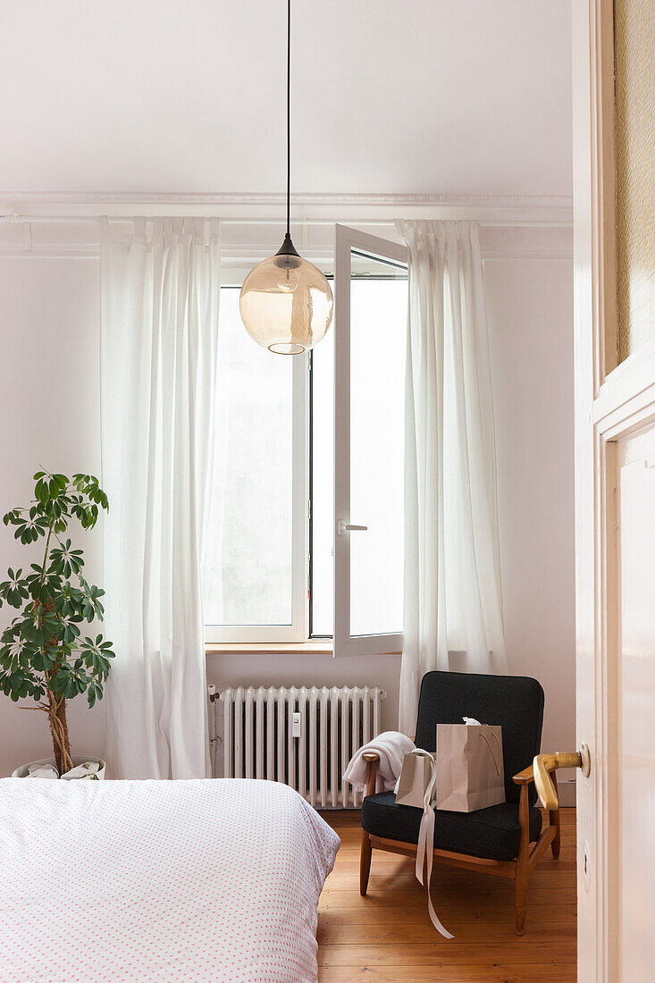 Schlafzimmer mit weißer Bettwäsche, schwarzem Sessel und Glas-Pendelleuchte