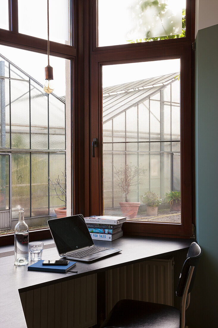 Arbeitsplatz mit Laptop am Fenster mit Blick auf Gewächshaus