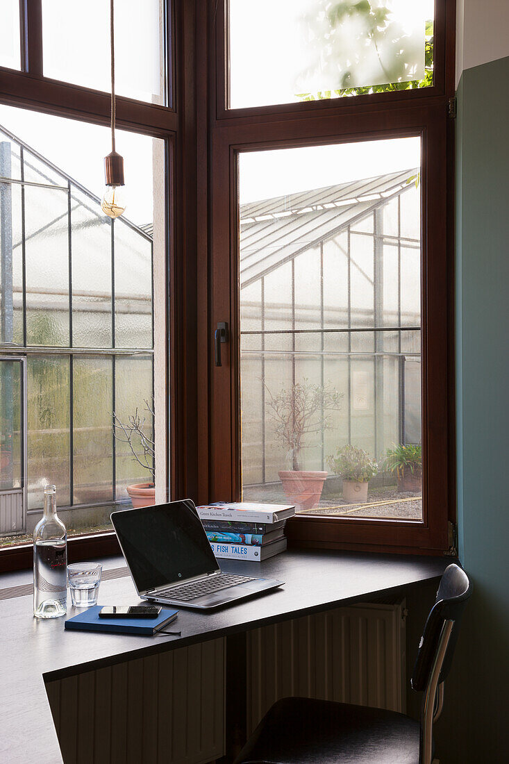 Workstation with laptop by the window with a view of the greenhouse