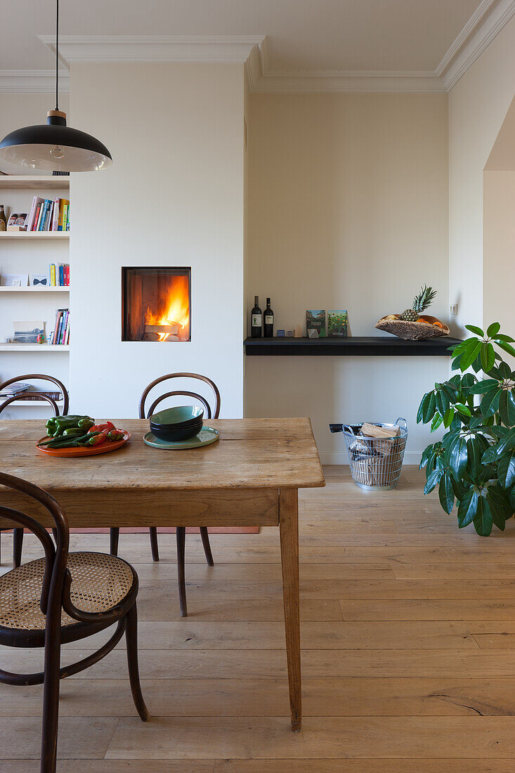 Holztisch und Rattanstühle im Esszimmer mit Kamin und Zimmerpflanze