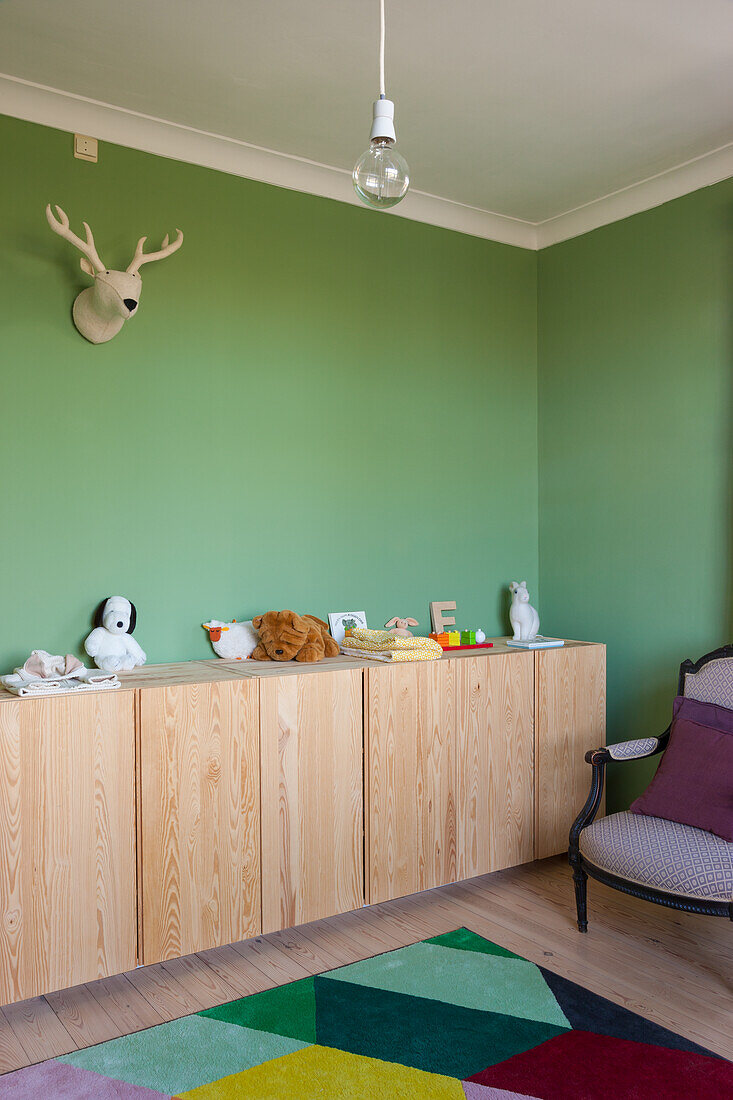 Wooden sideboard with toys in children's room with green walls and colorful carpet