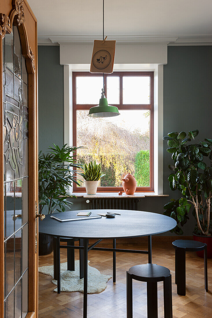 Round dining table with green pendant light and houseplants in front of the window