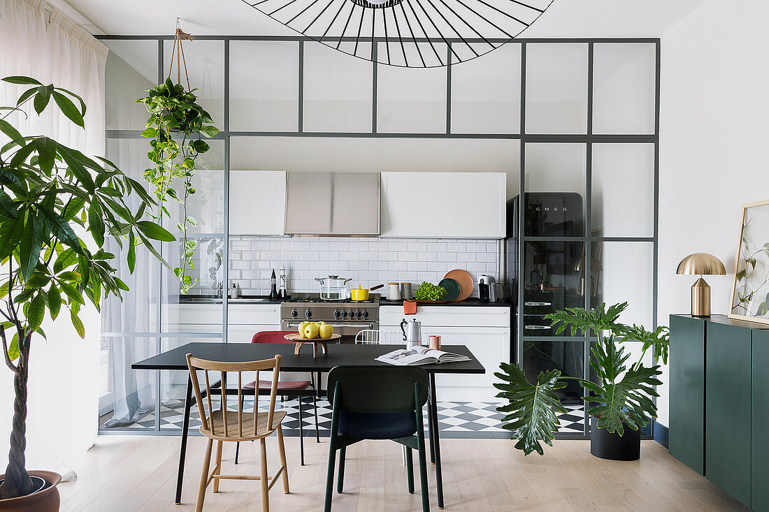 Esstisch mit verschiedenen Stühlen vor der Küche mit Glas-Stahl-Wand