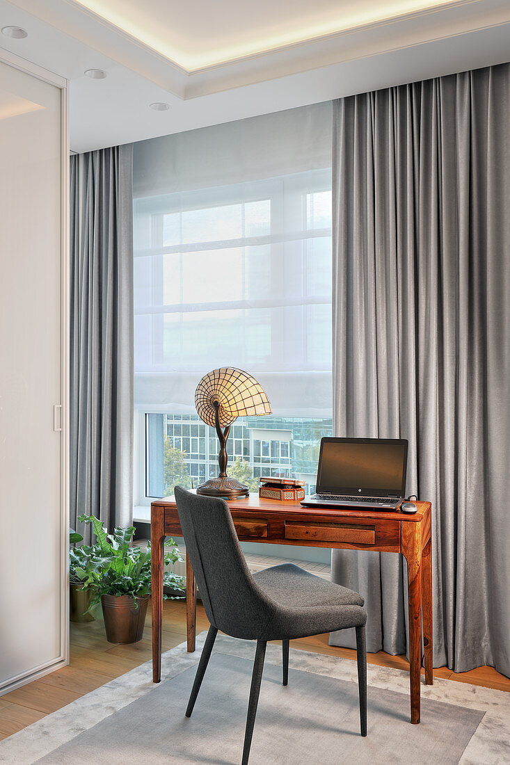Grey upholstered chair and desk opposite window with grey curtains