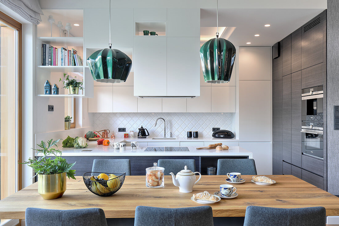 Upholstered chairs around wooden table in front of open-plan kitchen in white and grey