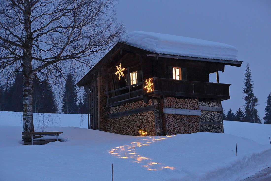 Beleuchteter Weg im Schnee zur alpinen Hütte am Abend