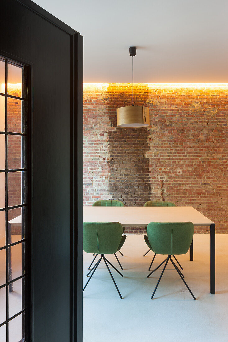 Dining area with green chairs, brick wall and indirect lighting