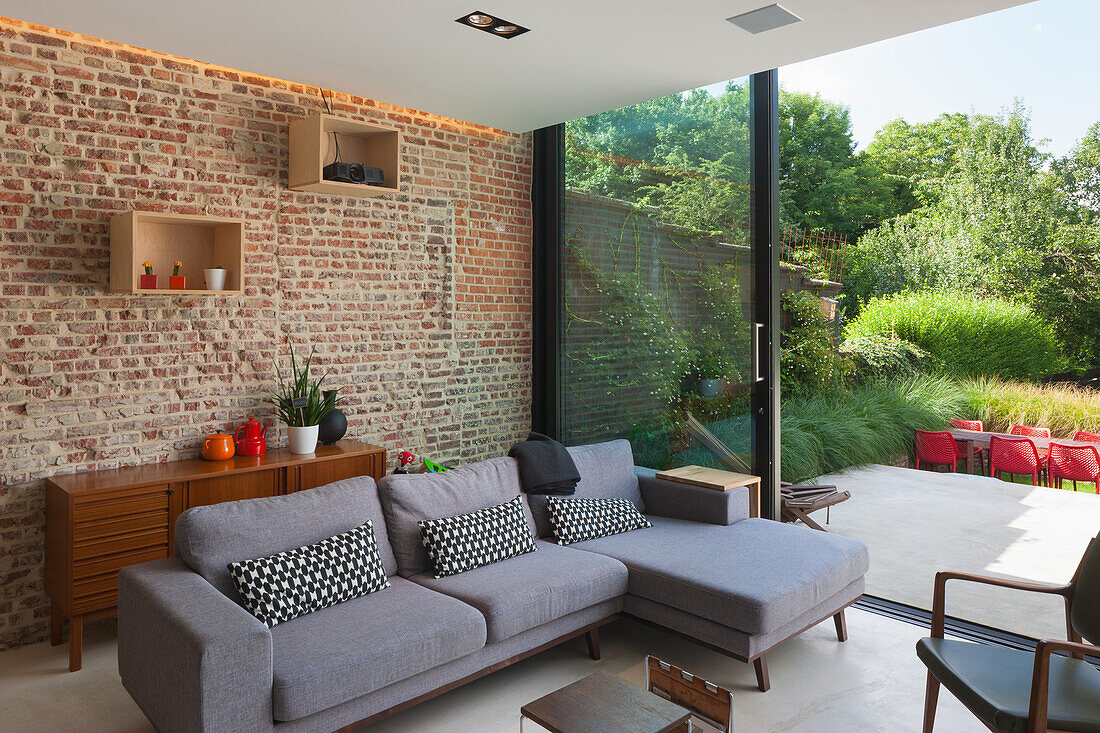 Living room with brick wall, grey corner sofa and garden view