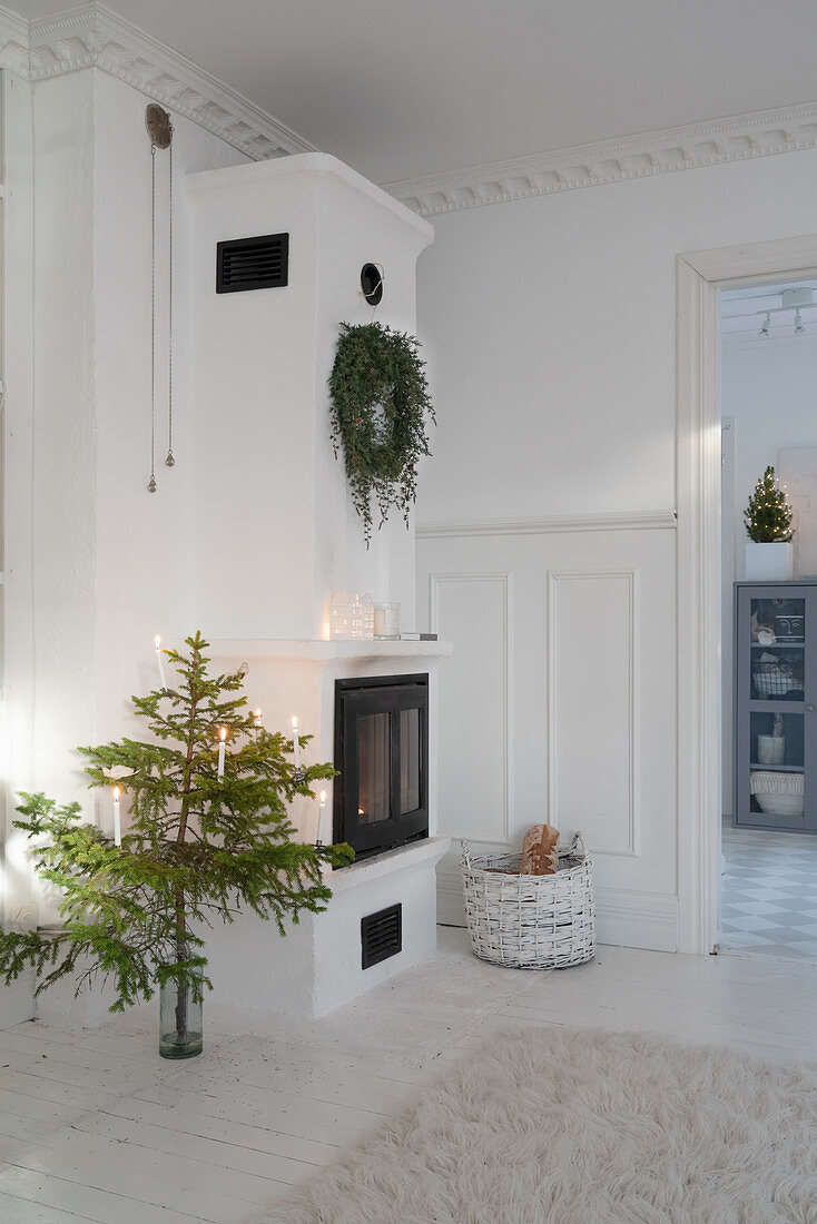 Small Christmas tree next to tiled stove in white living room