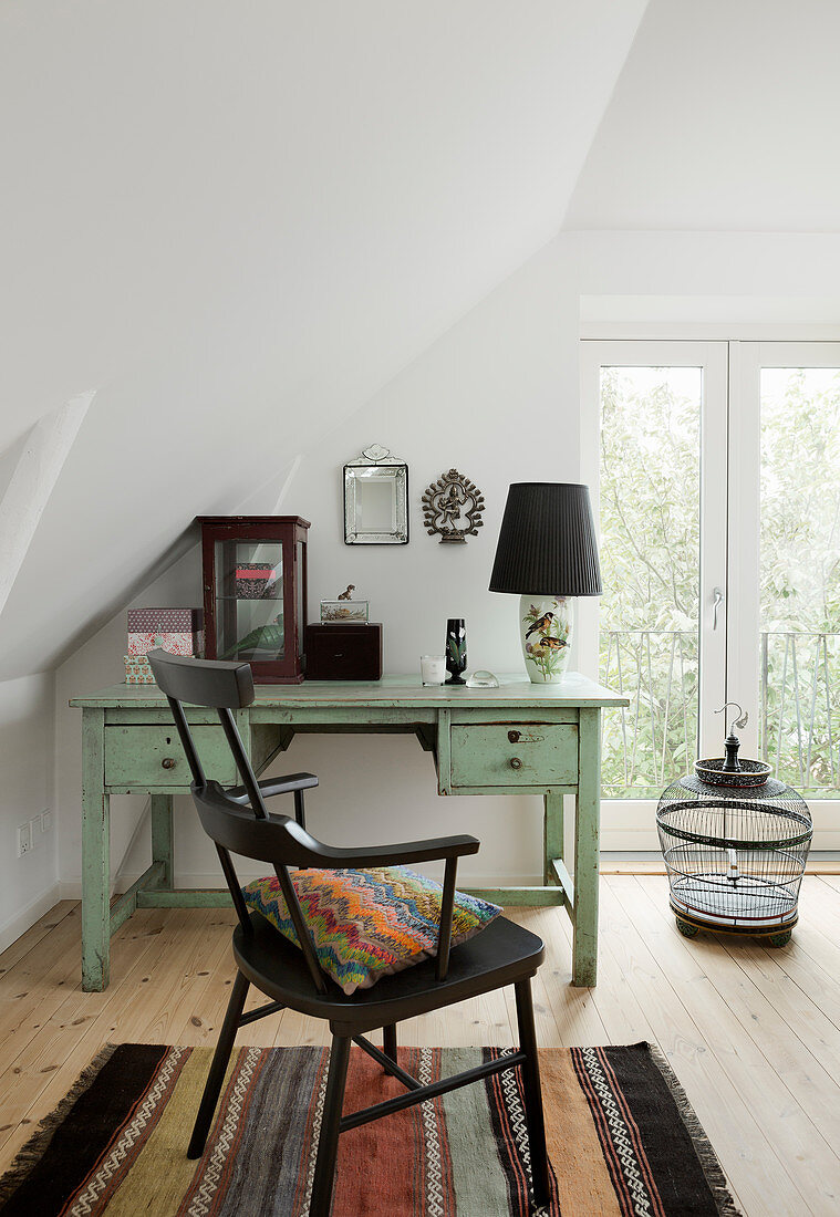Black chair at mint-green desk below sloping ceiling