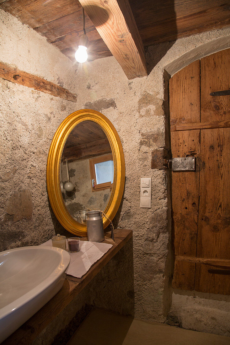 Oval, gilt-framed mirror in rustic bathroom of farmhouse