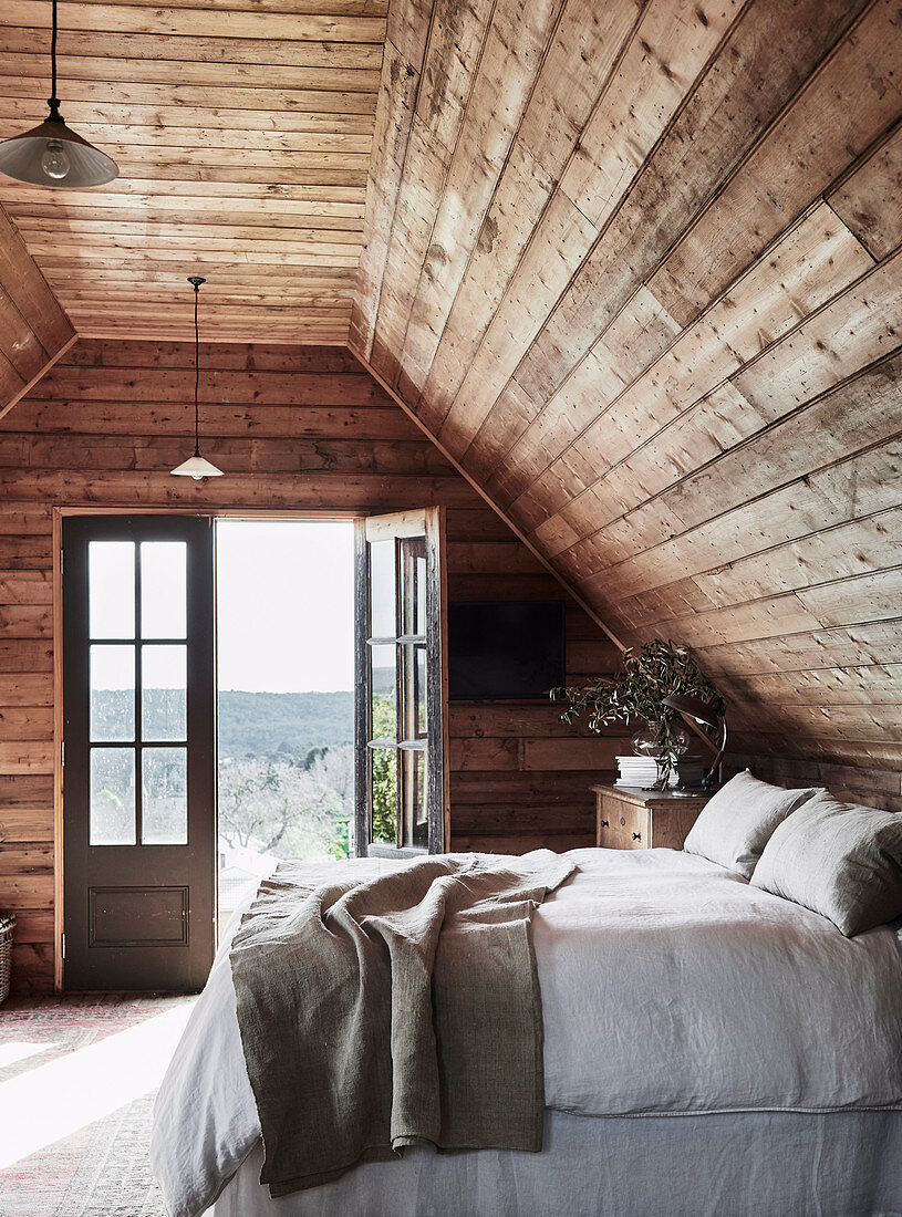 Doppelbett auf rustikalem Dachboden mit offener Balkontür