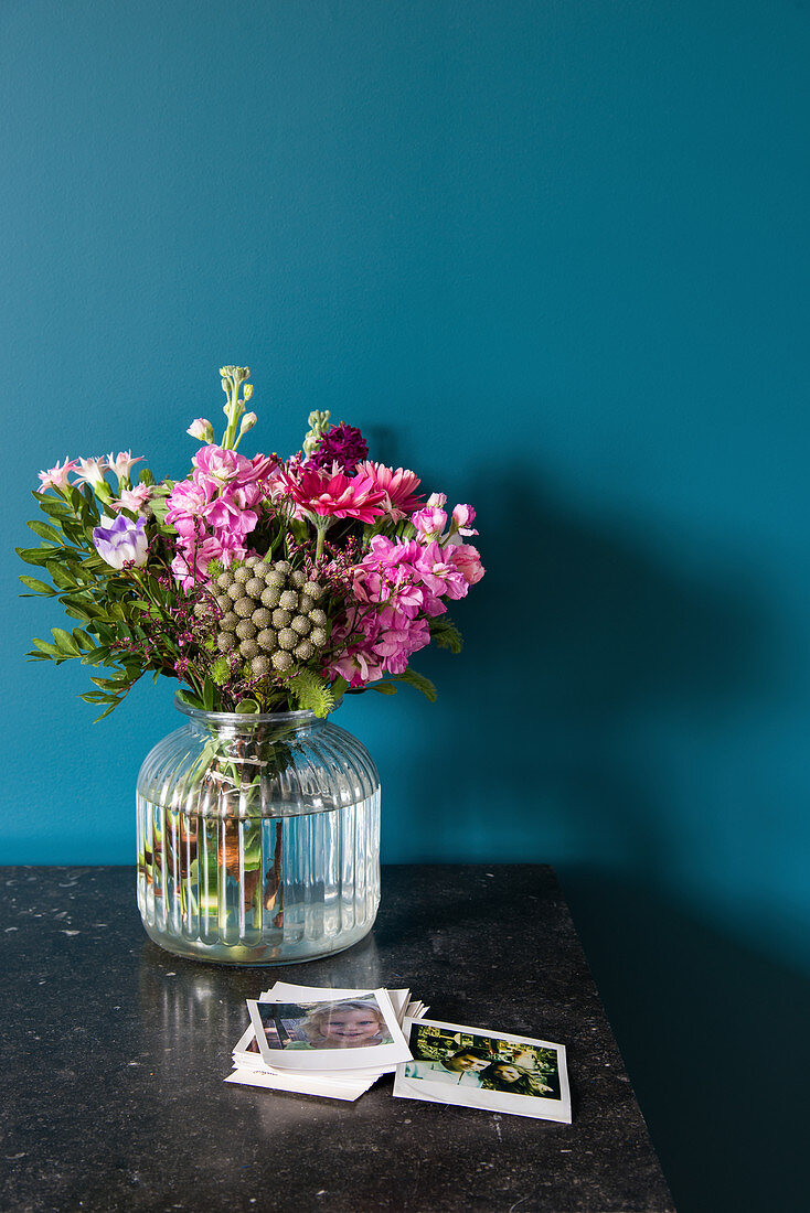 Glass vase of flowers against dark petrol-blue wall