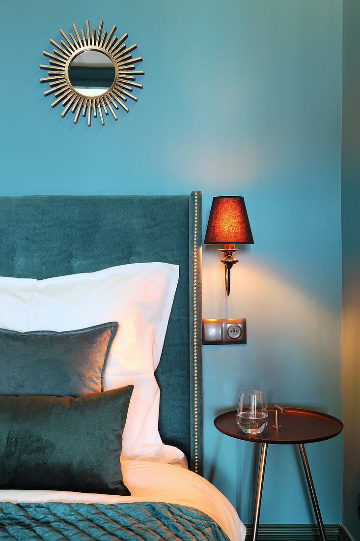 Sonnenspiegel an blauer Wand überm Bett mit Betthaupt