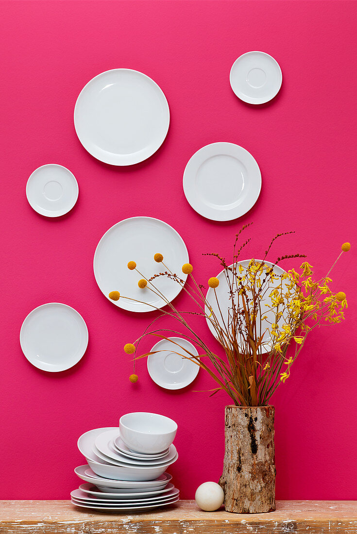White plates on hot-pink wall and yellow flowers in tree-stump vase
