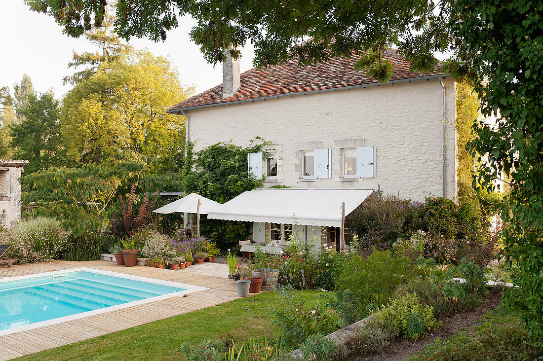 Outdoor swimming pool in the garden of converted French mill with awning, lawn and flower beds