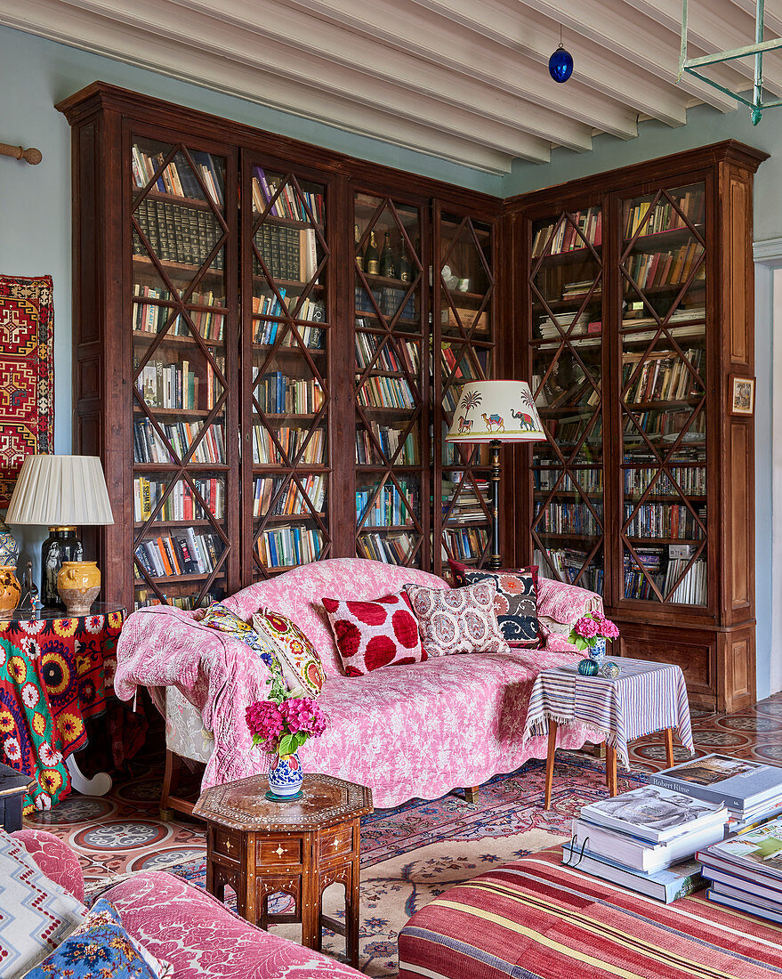 Sofa mit rosa Überwurf vor hohem, antikem Bücherregal