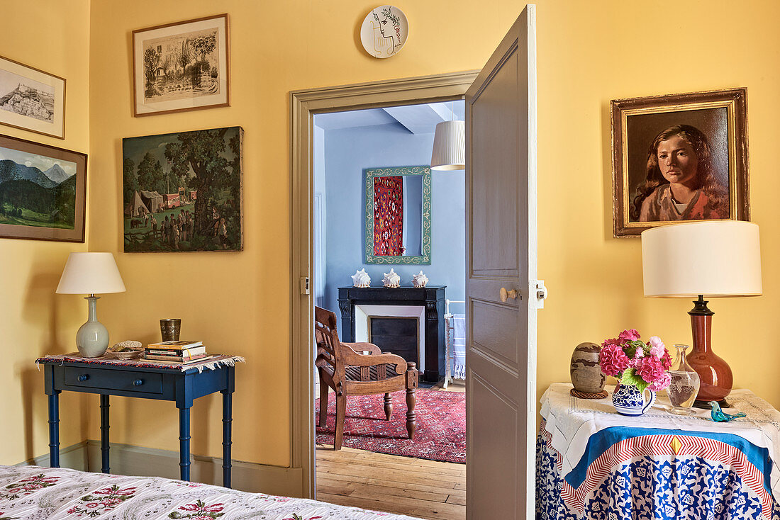 Artwork on yellow wall and view through doorway to carved wooden chair
