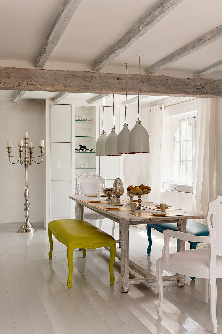 Large white pendant lights hanging above an antique cherry wood dining table with brightly coloured Louis benches and chairs