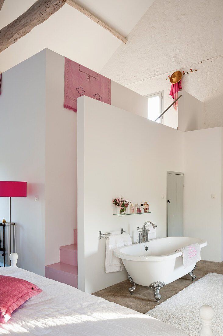 Freestanding bath in open plan bedroom with pink staircase