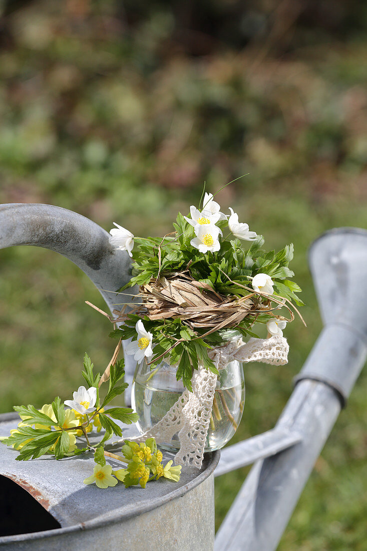 A small bouquet of wood anemones and primrose flowers with a grass cuff and lace ribbon, 