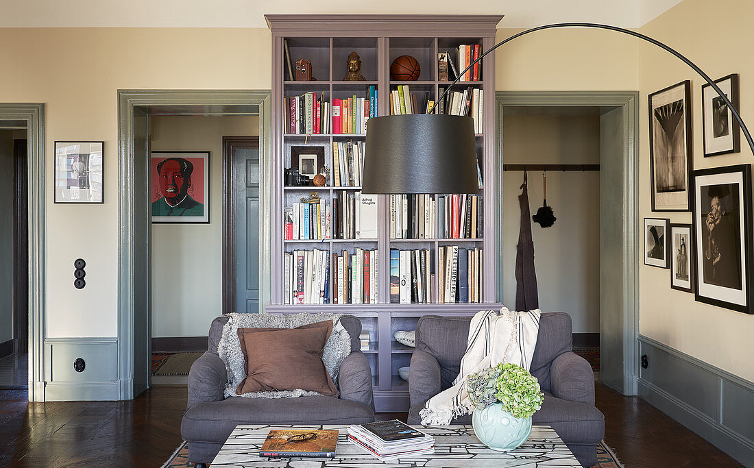 Graue Polstersessel, Couchtisch und Bogenlampe vor Bücherschrank