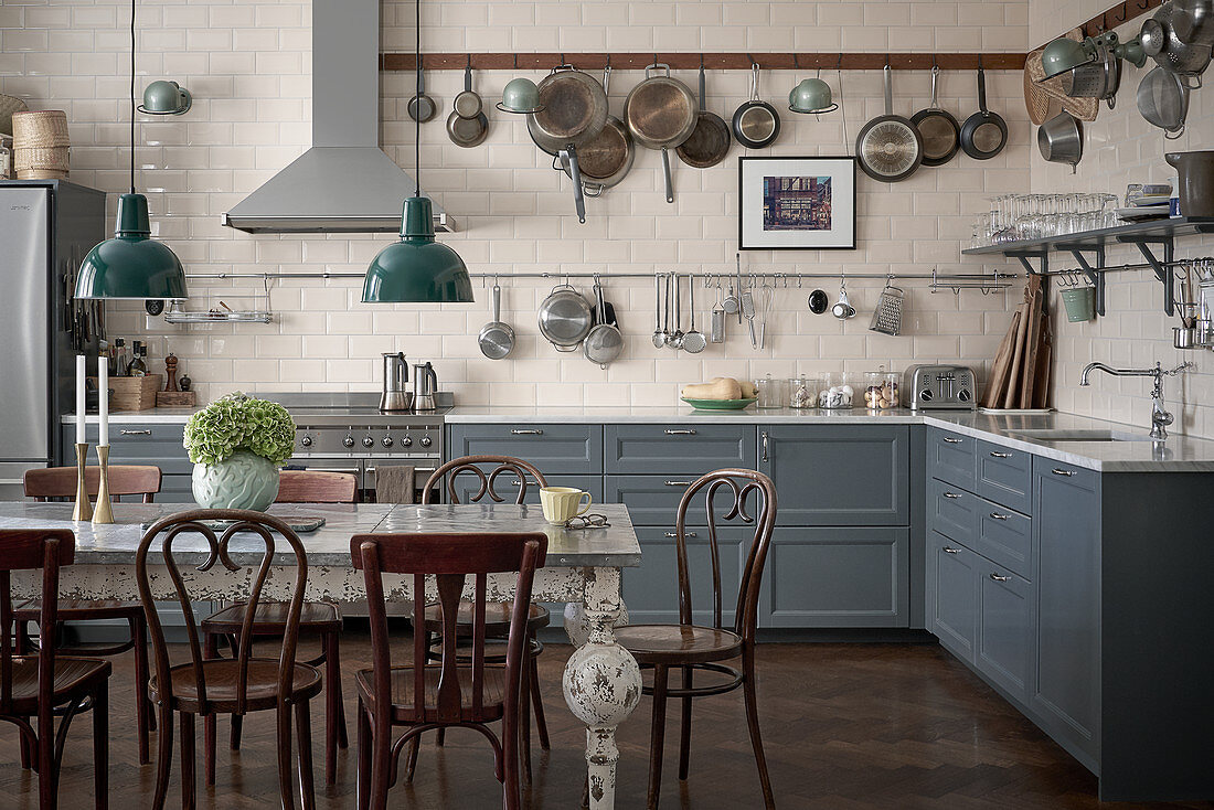 Pans hanging from rack above kitchen counter with grey cabinets and antique table in dining area